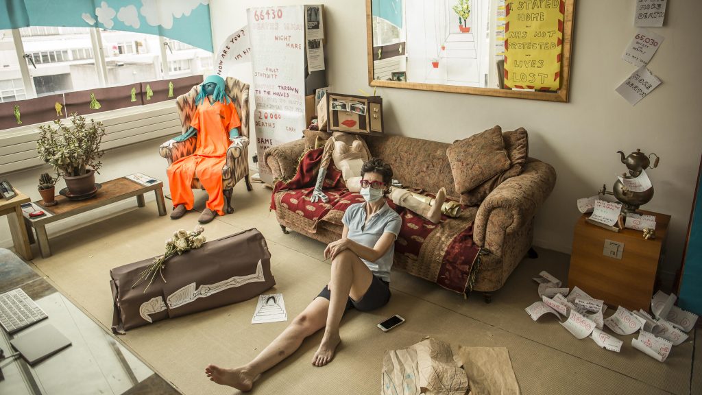 Im sitting - in my shorts - in my installation. Theres a prisoner in Guantanamo orange ranting on her phone, a coffin with the corpse shown rotting on the side, and a vulnerable naked woman lying on the sofa. Theres lots more not visible here.