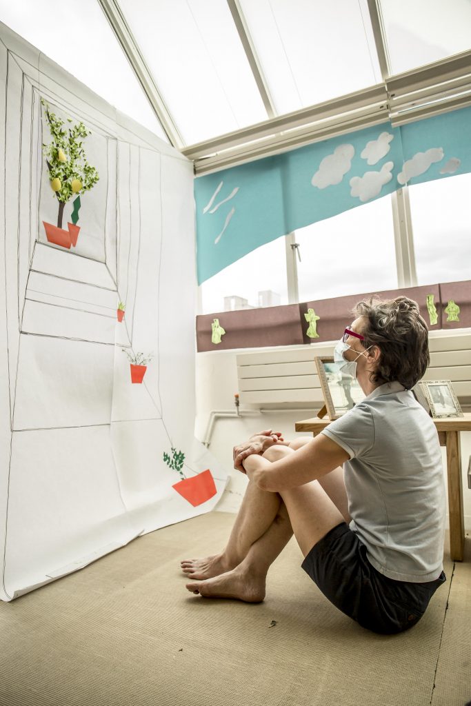 white woman in shorts sitting on the floor clasping her knees looking down a paper perspective tunnel at a paper tree loaded with luscious bulging lemons.