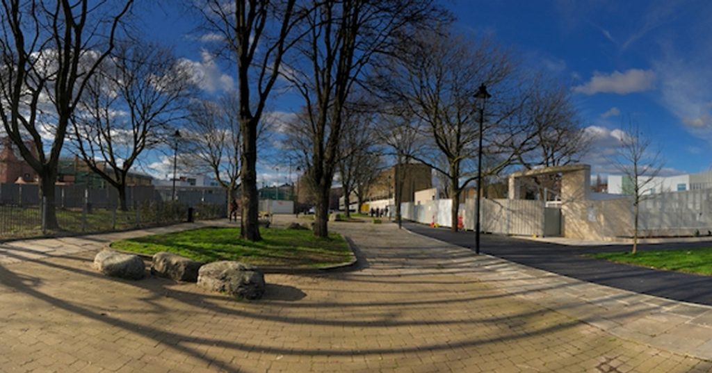 Scattered under a glorious blue sky, this photograph shows more and more trees as you look more and more closely. Alone with their wintry shadows, they’re each marooned without the buildings they were surely planted alongside.  Behind three fat, flat boulders, concrete tracks lead - is it nowhere?  To the right, pale walls trap white buildings. 