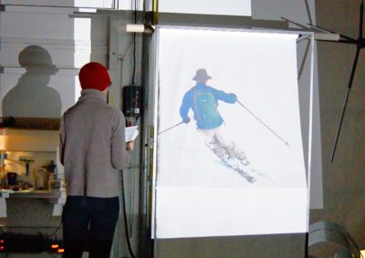 On the left, a woman faces away from the audience and towards a projection of a man skiing fast